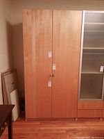 Closed front view of light beech two-door cabinet with metal swirl handles.