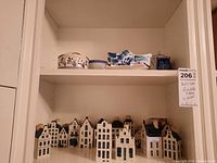 Overview: top shelf shows Delft shoe figurine, covered pot, plate and teapot; bottom shelf shows 15 Delft house decanters