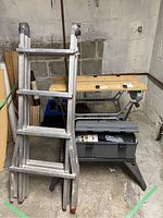 Workmate work table, extendable ladder, and plastic toolbox grouped together in a basement setting
