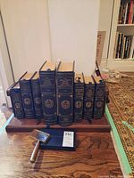 Full arrangement of eight leather-bound volumes on wooden display shelf with metal supports, magnifier in front