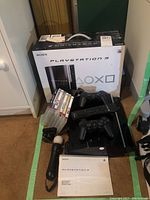 Photo showing PlayStation 3 console, controllers, game discs, remote, instruction manual, and original box.