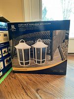 Front view photo of the Acoustic Research portable wireless speaker set in original box showing two white lantern-style speakers with black mesh panels indoors.