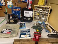 Photo showing Craftsman jig saw, hardware organizer bins, and various small tools and screws on a table against a pegboard wall.