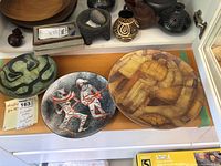 Three round vessels: green/black ceramic plate at left, speckled enamel bowl center, brown/yellow ceramic plate right on white surface