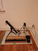 Full view of telescope mounted on a tripod with additional tripods and carrying case on floor.