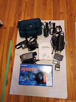 Overall lot laid out on white backdrop showing two camcorders, box, bag, manual and cables