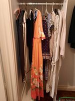 Side view of various vintage dresses on hangers in closet including black, orange floral, polka dot print and cream colored garments