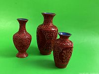 Three cinnabar vases arranged side by side showing varying sizes and red cinnabar lacquer with detailed engravings.