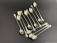 Twelve sterling silver spoons arranged on black surface