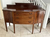 Full front view showing mahogany sideboard with three drawers and two hinged cupboard doors on tapering legs, raised back edge on top.