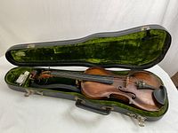 Open hard shell case with green velvet interior showing violin seated inside