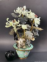 Full view of enamelled cloisonné planter with carved jade flower arrangement and metal leaves on black backdrop