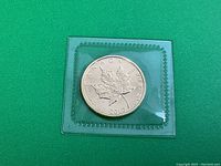 Reverse of coin showing maple leaf design and weight inscription in clear plastic holder on green background