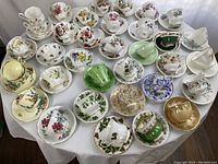 Full view of table covered with 24 assorted bone china tea cups and saucers in multiple patterns