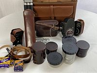 Overview of brown leather camera bag with contents displayed: two cameras, tripod, lenses, filters and light meters