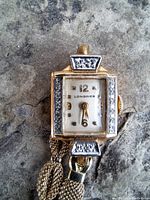 Front view of watch showing rectangular dial, gold-tone numerals and diamond-set bezel.