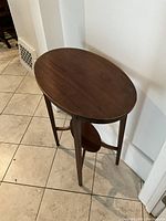 Full view of an oval wooden side table with four tapered legs and lower oval shelf.
