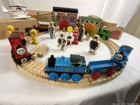 Circular layout of track assembled with three locomotives, two carriages, figures, signs, trees and station facade
