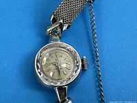 Frontal view of watch face and attached mesh bracelet against blue background