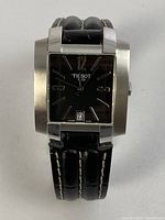Front view of watch showing square stainless steel case, black dial, applied numerals, date window at 6 o’clock