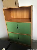Full frontal view of the cabinet showing green doors on bottom two shelves and open top shelf.