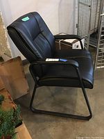 Side view showing padded black faux leather seat and backrest with armrests and metal sled base