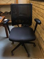 Front view of the black office chair showing mesh backrest, padded armrests, and fabric seat.