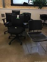Six office chairs arranged in a warehouse setting showing variety in style, including adjustable chairs with wheels and simpler metal framed chairs without wheels.