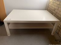 Photo from above and side showing full table and lower shelf in white laminate wood.