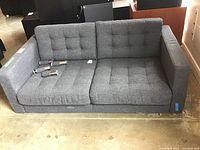 Front view of grey sofa with loose tufted seat and back cushions and detached legs placed on seat