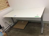 Front view of the IKEA Galant desk showing white laminate top and grey metal legs, situated against a wall.