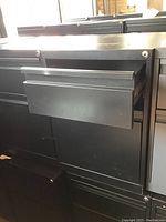 Close-up of a black metal filing cabinet drawer pulled out showing two drawers, both with simple metal handles