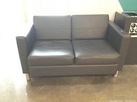Dark brown two-seater love seat in faux leather upholstery with metal legs shown from the front in bright lighting.
