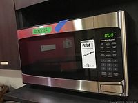 Front view of the Hamilton Beach microwave showing stainless steel front, black door with window, and digital keypad.