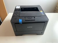 Front view of black Brother printer showing brand logo and top paper output tray