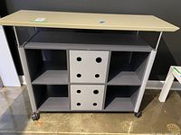 Front angle view of metal rolling table showing top surface, shelves, and storage boxes.