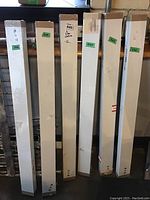 Long narrow boxes containing IKEA shelving units, packaged and sealed, stacked upright against wall.