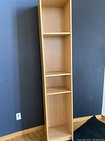 Front view of the tall wood laminate shelving unit against a dark wall, showing four vertical sections with three shelves, two shelves are adjustable.