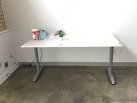 Front view of white Ikea Galant desk with laminate top and silver metal legs, situated in corner of room with outlets visible on walls.