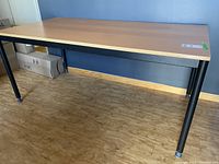 Table showing wood grain finish top with beveled edge and black trim, viewed from angle.