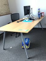 Photo showing left side and top of rectangular laminate office table with metal legs and office chair beside it.