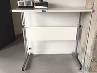Front view of adjustable height table, white melamine top, metal legs with adjustment knobs and white modesty panel underneath.
