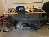 IKEA Galant table with light wood melamine top and silver metal legs placed in an office setting with laptops and various cables on and under it.