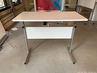 Front view of a height adjustable table with rectangular white laminate top and silver metal frame base.