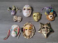 Top-down view of 8 ceramic masks arranged on a grey wood surface