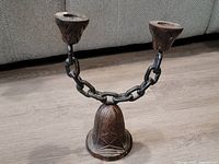 Front angled view of brutalist style candle holder sculpture made from wood and metal chain, showing carved wood base and two candle cups connected by metal chain.