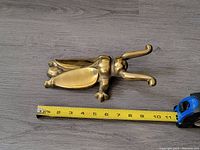 Top view of brass beetle boot jack placed next to a measuring tape showing approximately 10 inches in length.