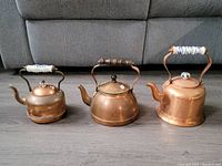 Group shot of three copper kettles showing various sizes and handle styles.