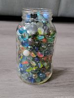 Glass jar filled to capacity with vintage multicolored marbles, showing size and quantity in container