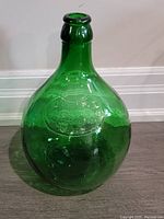 Full view of the large green glass demijohn bottle showing its shape and color.